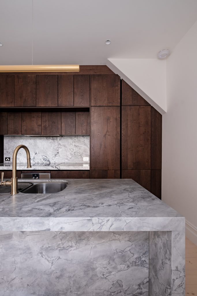 Marble island with a brass tap in front of dark oak cabinetry