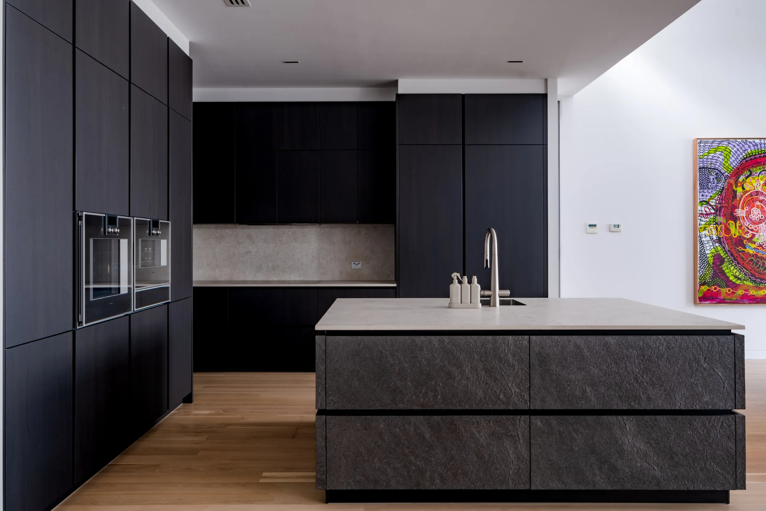 Custom luxury Häcker kitchen featuring matte black timber handleless cabinetry, beige stone benchtops and splashback, and a kitchen island with premium stone cabinet fronts.