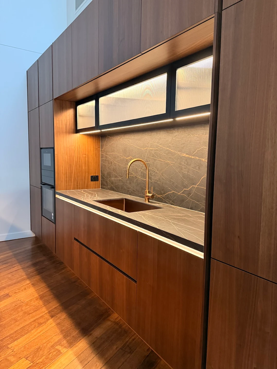 Luxury Häcker kitchen featuring warm premium oak timber cabinetry, handleless cabinet fronts, and premium black marble bench tops and splashback with gold veining.